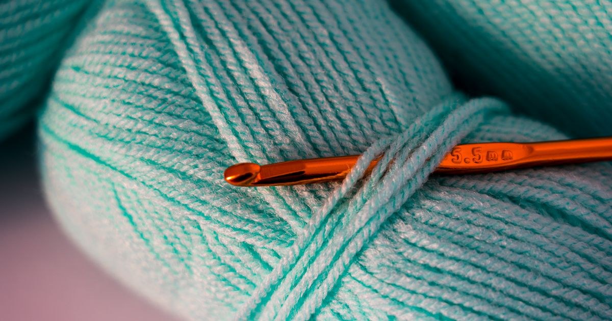 Macro photograph of teal yarn with a crochet hook, highlighting texture and detail.