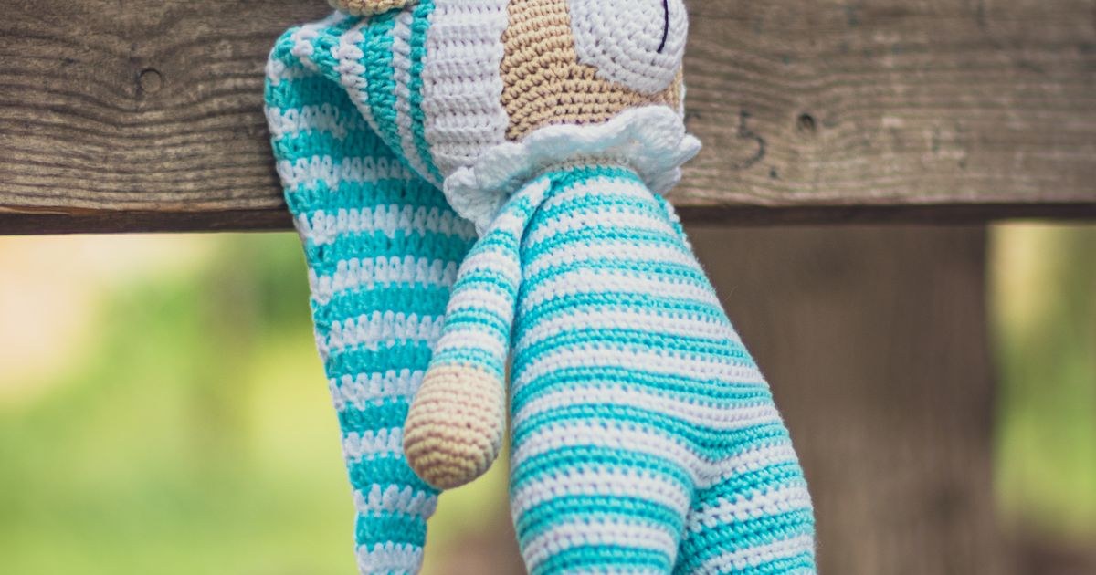 Colorful crochet teddy bear draped over a rustic wooden bench outdoors.
