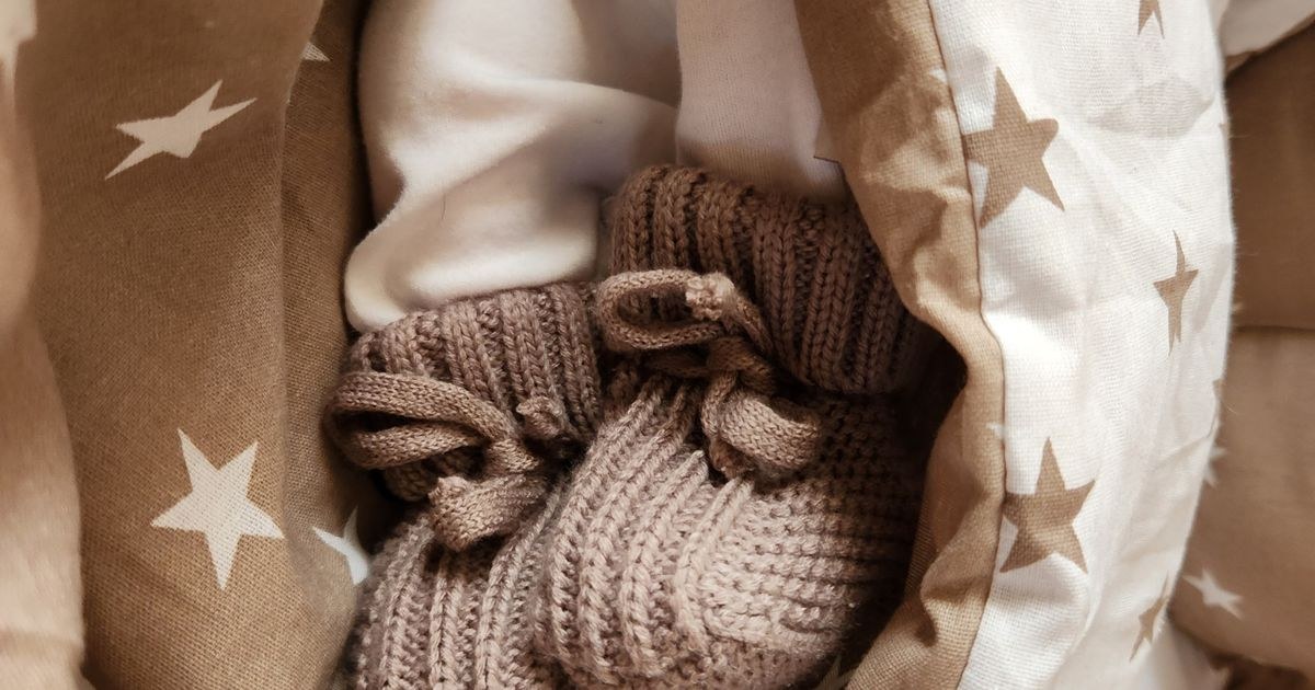 A newborn baby wearing knitted booties, nestled warmly in a star-patterned blanket.