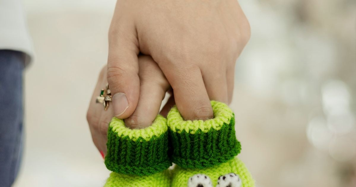 Green crocheted baby booties held by parents