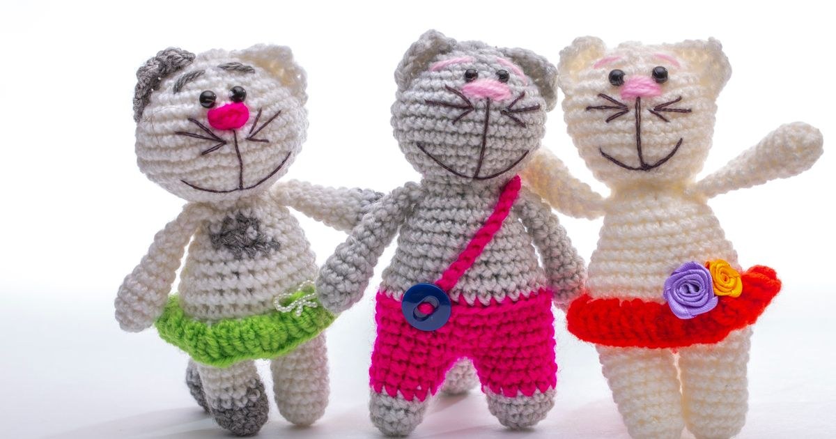 Three colorful crocheted cat dolls with unique outfits against a white background, showcasing craft artistry.