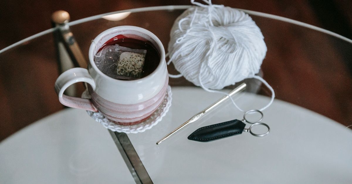 A cozy setup featuring tea and crochet materials on a glass table for a relaxing creative moment.