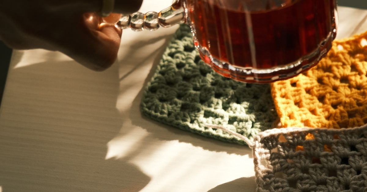 Warm sunlight on hands holding tea with crochet coasters. Perfect for cozy moments.