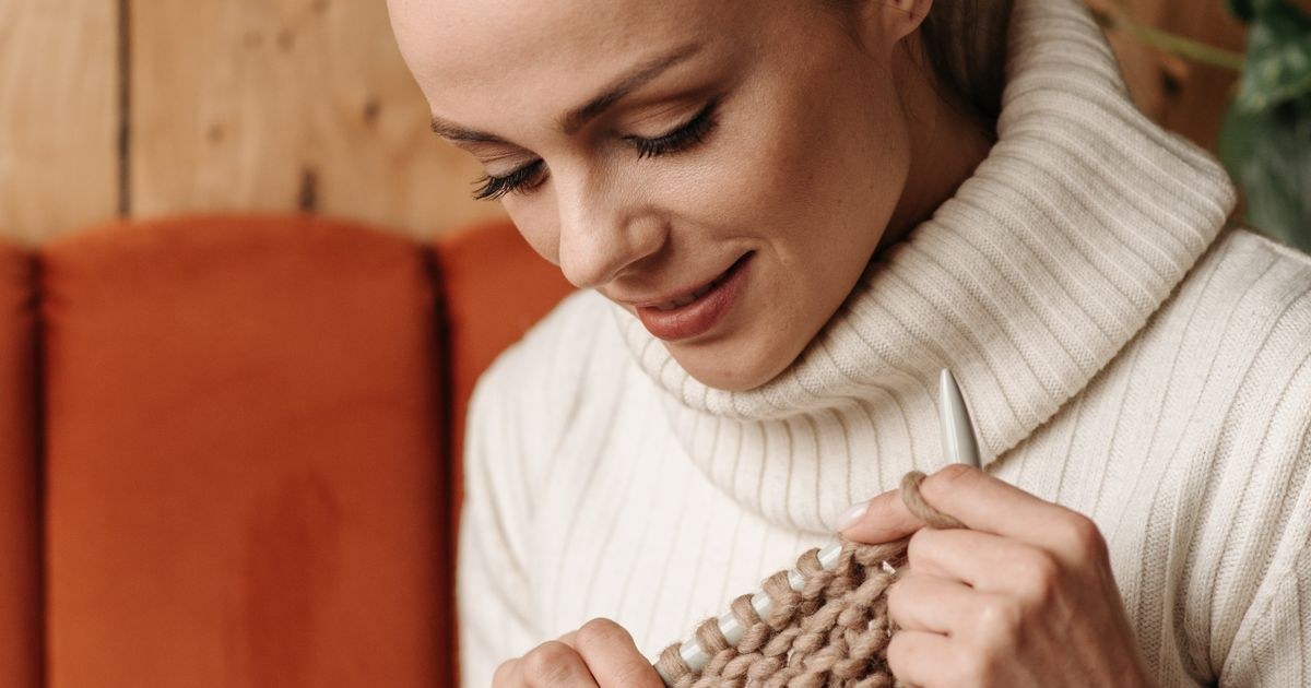 A woman knitting with chunky yarn indoors, creating a cozy and warm atmosphere.