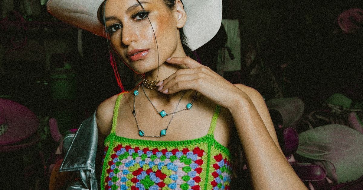 Stylish woman in crocheted top and cowboy hat posing indoors.
