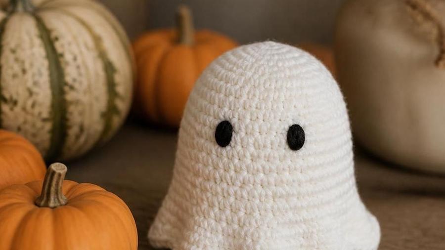 A small white crochet ghost amigurumi with a scalloped wavy bottom edge and a simple embroidered face.
