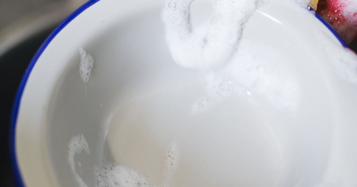 Vibrant photo of washing a bowl with a yellow sponge and soap bubbles.