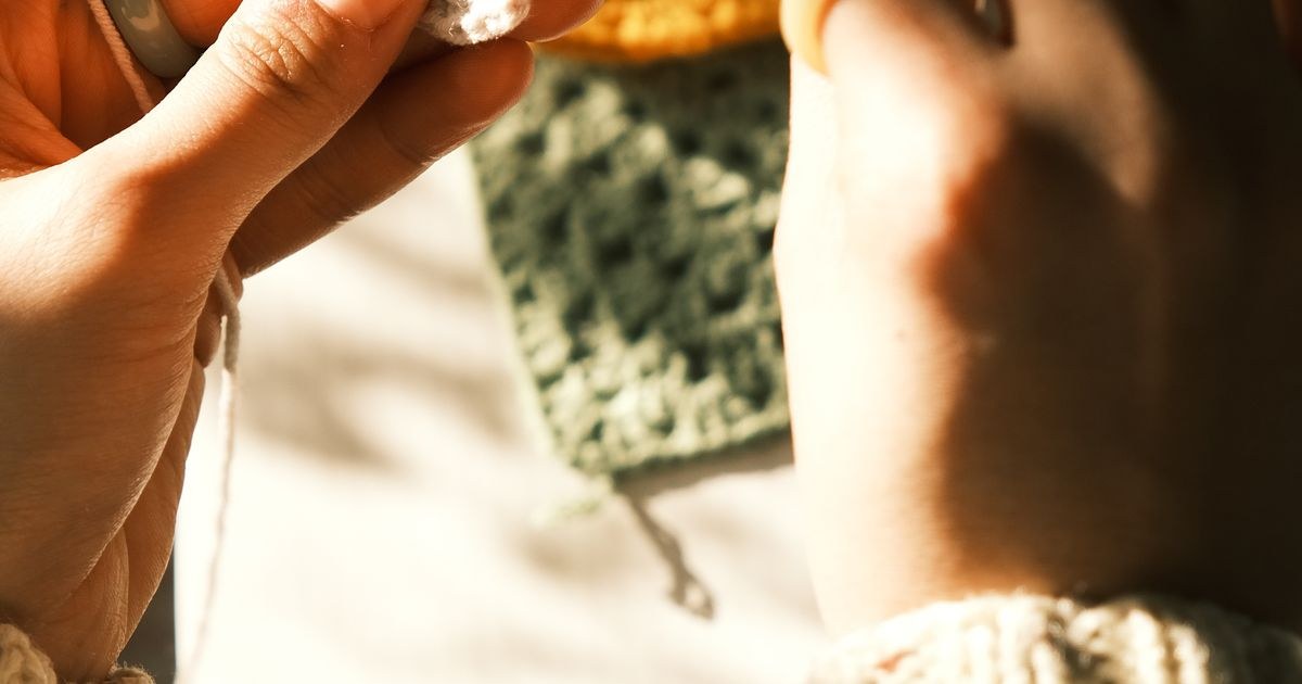 Detailed view of hands crocheting colorful squares by sunlight.