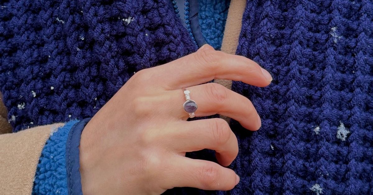 Hand with engagement ring wrapped in blue winter scarf, snowflakes sprinkled.