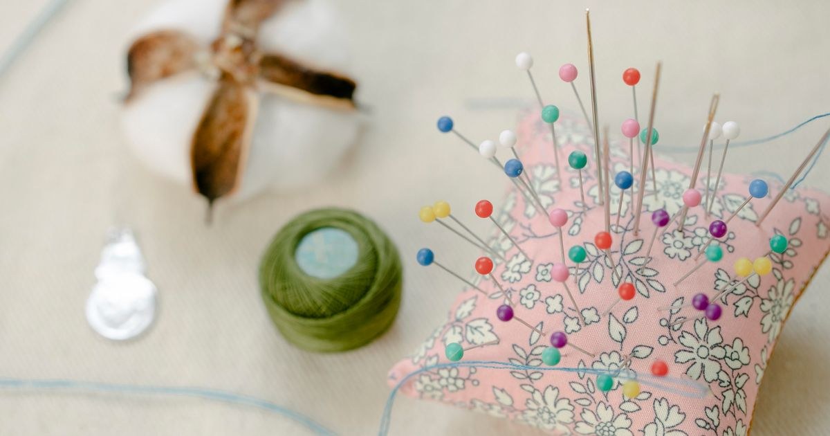 From above colorful pins attached to small pillow placed on table with thread roll and cotton ball in workshop