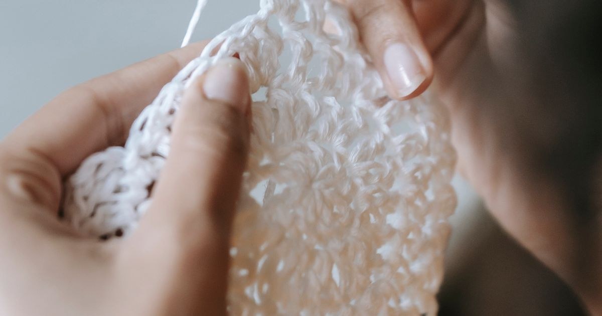 Detailed shot of hands skillfully crocheting with a hook and white yarn, showing the working tension.