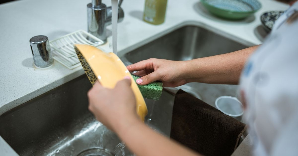 Close-up of hands hand-washing an item gently in a sink with running water.