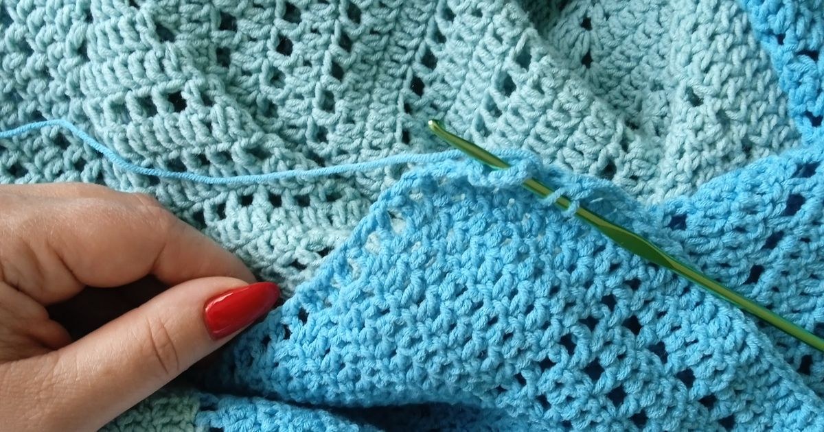 Close-up of hands crafting a knit blanket with vibrant blue yarn, finishing the edge.