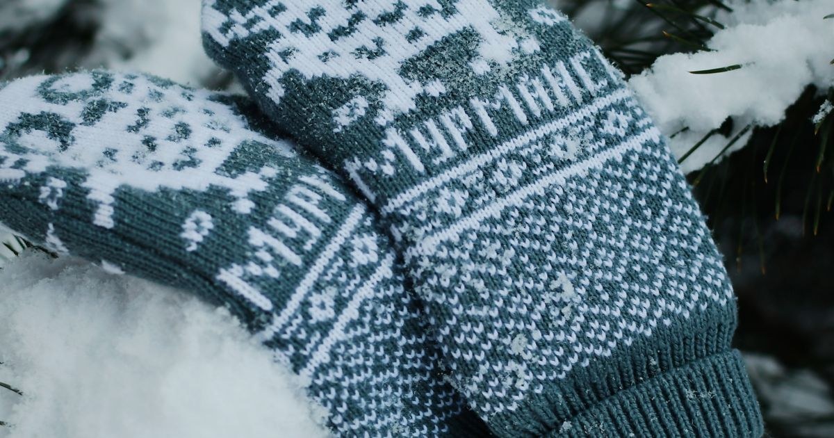 Warm knitted mittens on snowy pine branches, capturing winter coziness outdoors.