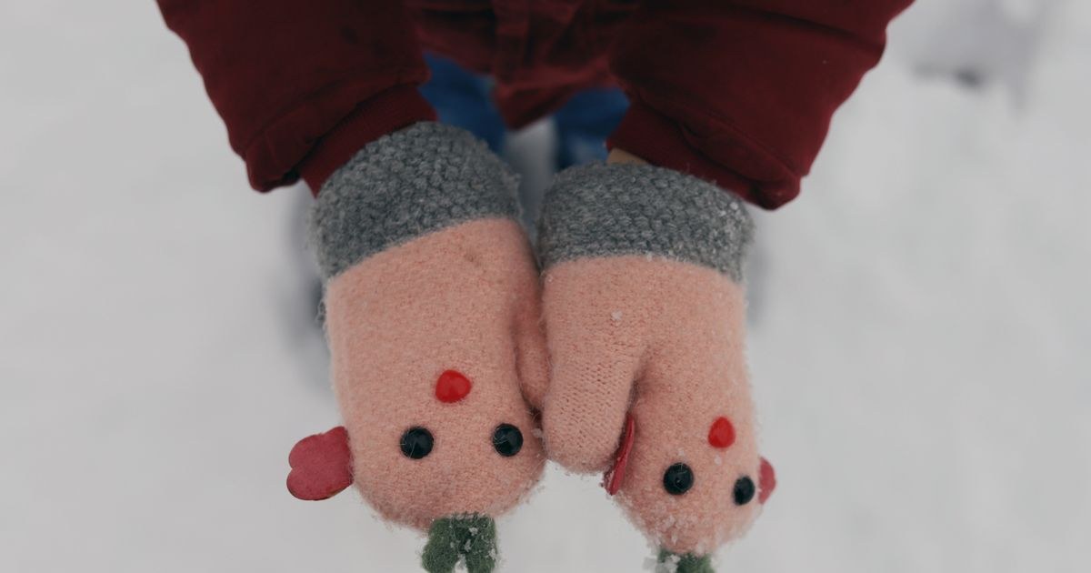 Adorable child's hands in cute mittens outdoors during winter snowfall.