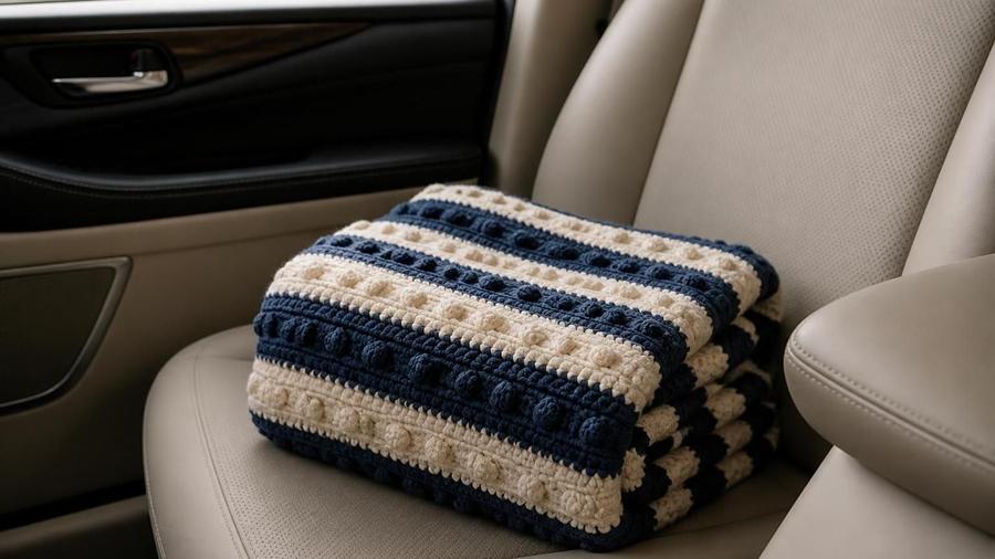 A folded navy and cream striped crochet lapghan with a raised bobble accent row, sitting on a car seat.
