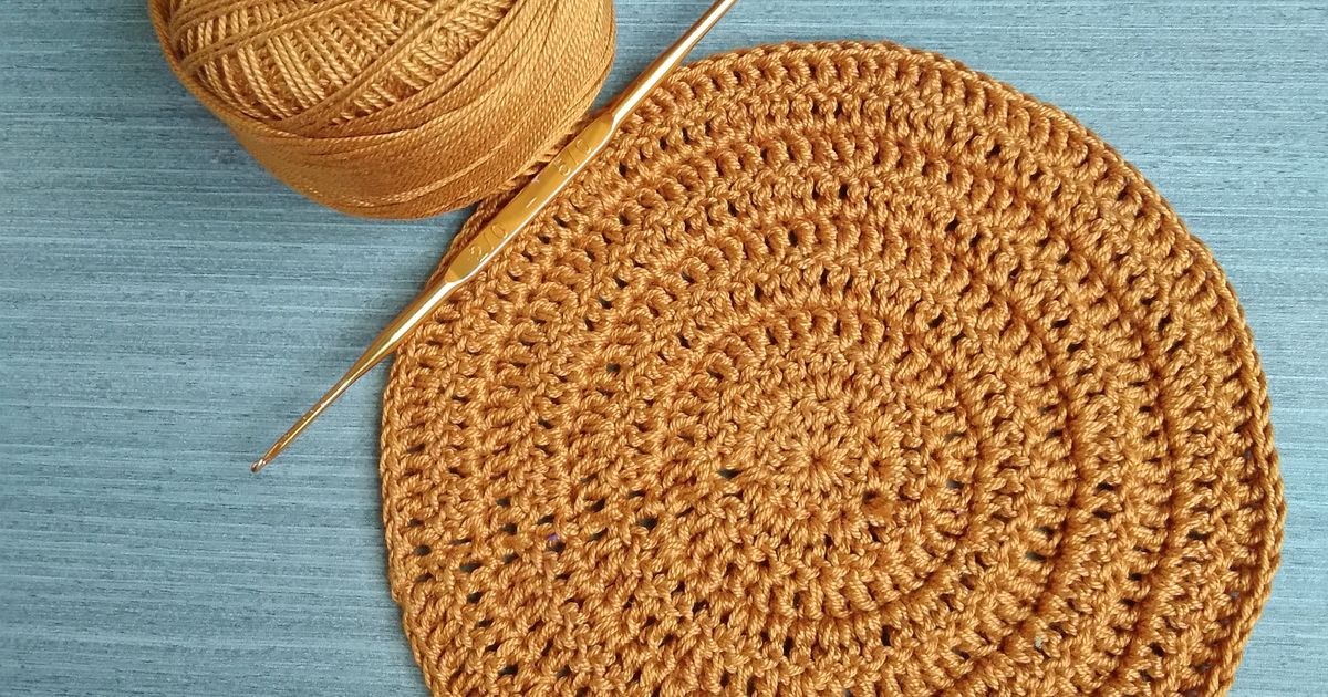 Close-up of a crochet circle with yarn roll and hook on blue background.