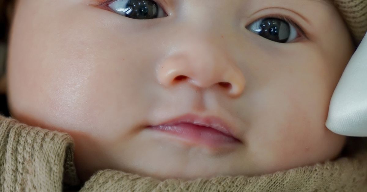 Adorable baby wearing a beige knit outfit and hat, with gentle expression.