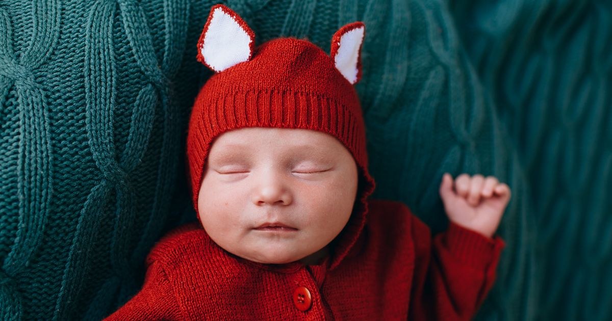 Top view of cute small infant in bright red warm costume on blue woolen blanket