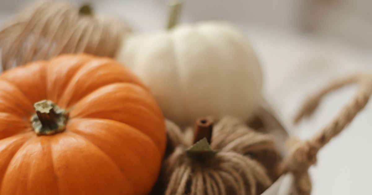 Cozy fall scene with pumpkins and wool decor in a woven basket, ideal for seasonal themes.