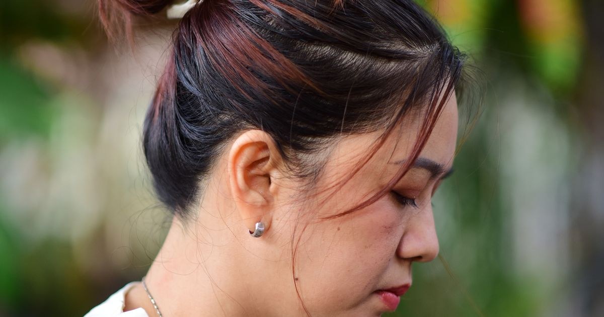 Close-up of a woman with a white scrunchie against a lush green background.