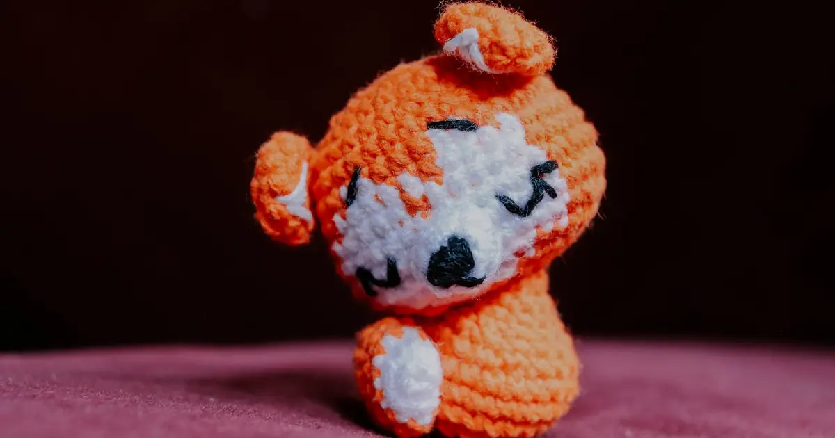 Adorable handmade orange crochet animal figure on a soft pink surface.