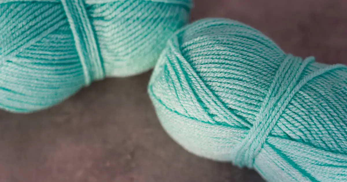 Close-up of two turquoise yarn balls on a textured surface.