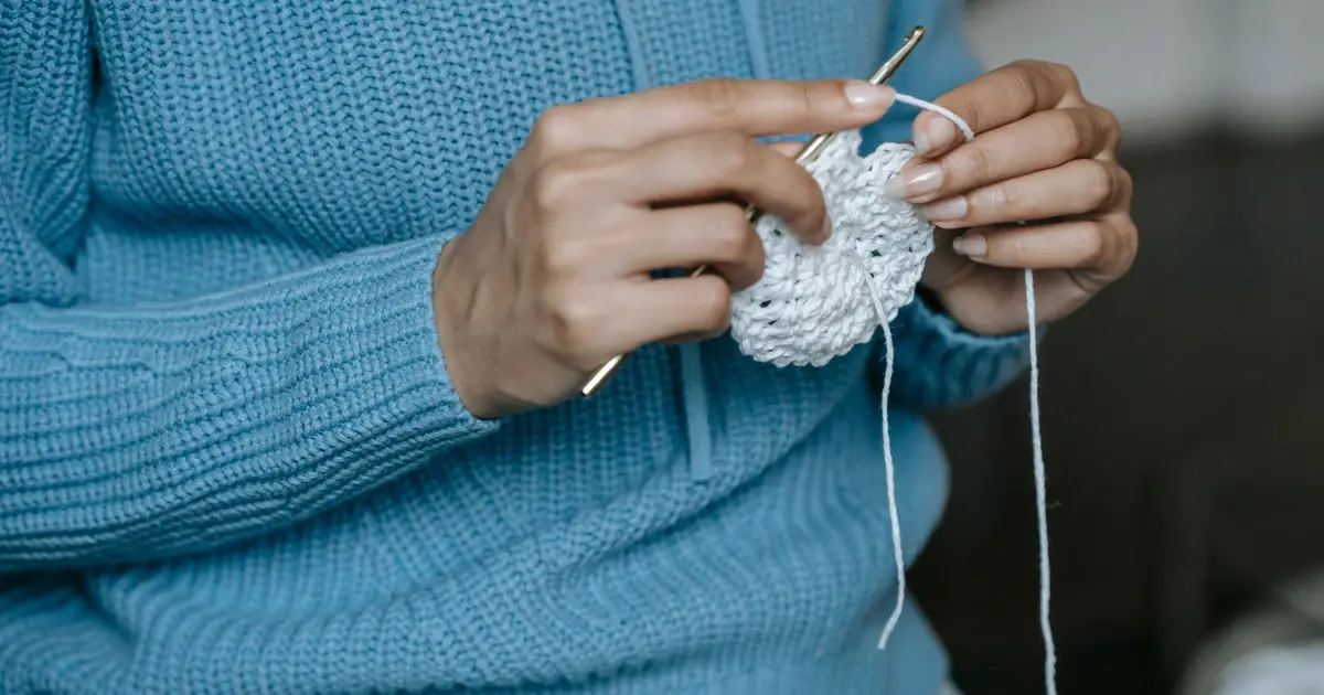 A person skillfully crochets a white yarn piece, showcasing the art of handmade craft.